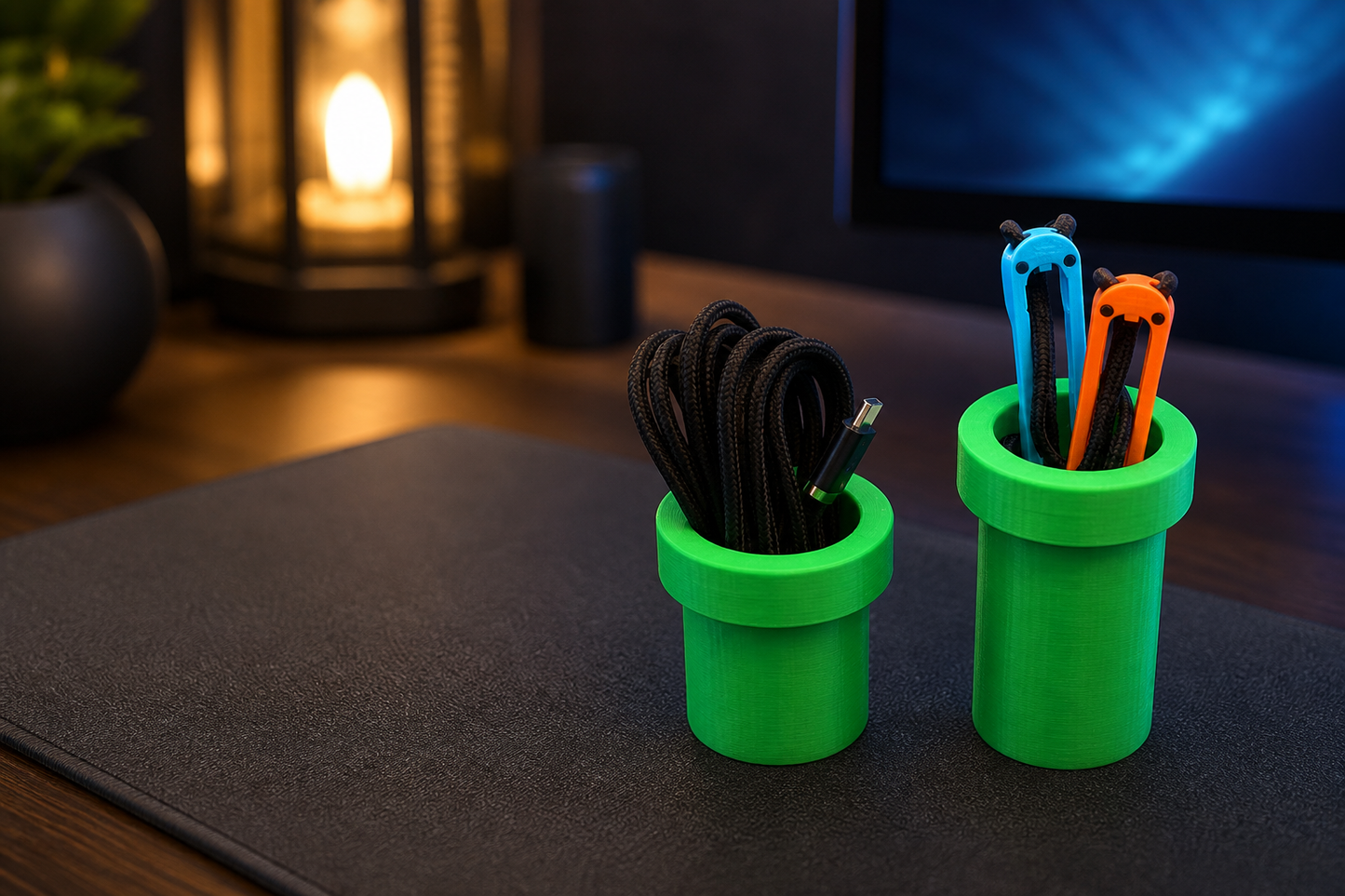 Green pipe-style magnetic cable organizers on a gaming desk holding a USB-C cable and blue and orange cable clips